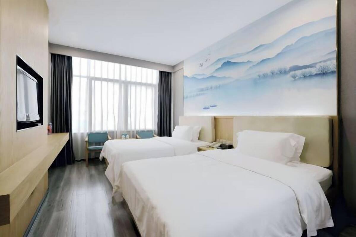 Quarto de hotel com duas camas, uma escrivaninha, uma cadeira, uma televisão e uma pintura de uma paisagem montanhosa.
