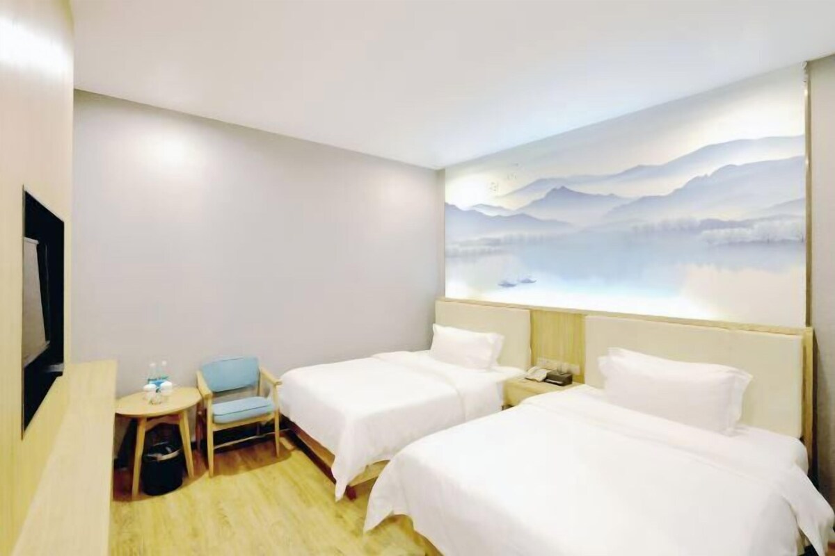 Quarto de hotel com duas camas, uma pequena escrivaninha com cadeira, televisão e um mural na parede.