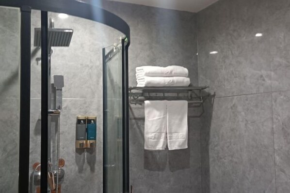 Uma casa de banho moderna com cabine de chuveiro em vidro, porta-toalhas com toalhas dobradas e dispensador de sabonete fixado na parede.