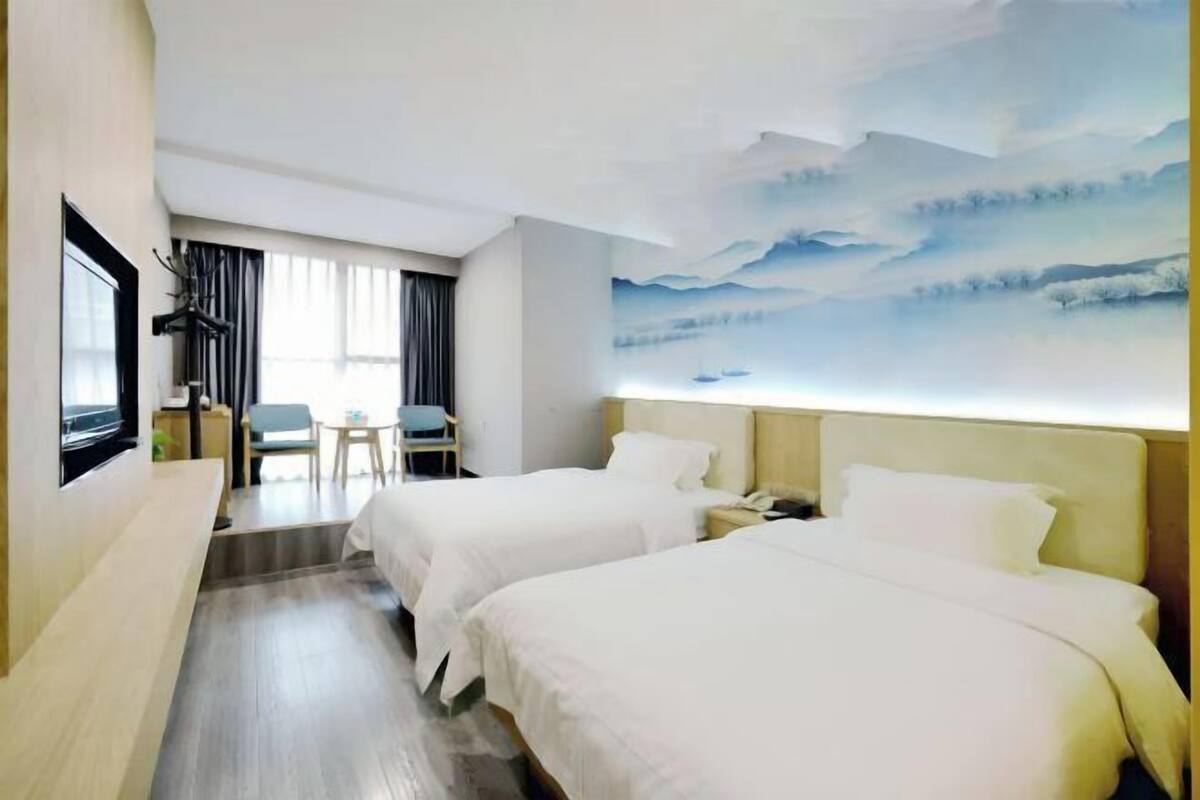Quarto de hotel com duas camas, uma escrivaninha, uma cadeira, uma TV e um quadro grande na parede.