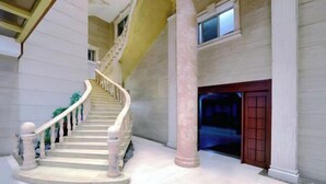 Μια επιβλητική σκάλα με μαρμάρινα σκαλοπάτια και λευκά κάγκελα, που οδηγεί σε μια σκοτεινή πόρτα.