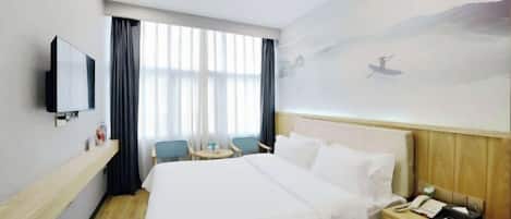 A hotel room with a bed, a bedside table with a phone, a TV mounted on the wall, a small table with chairs, and a window with curtains.