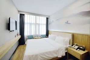 Quarto de hotel com cama, mesa de cabeceira com telefone, televisão na parede, pequena mesa com cadeiras e janela com cortinas.