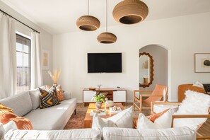 A modern living room with a sofa, armchairs, a coffee table, and a TV mounted on the wall.