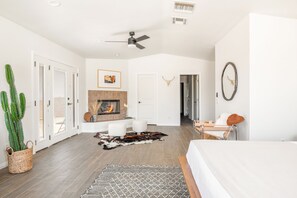 A spacious bedroom with a large bed, a ceiling fan, a fireplace, and a cactus plant.