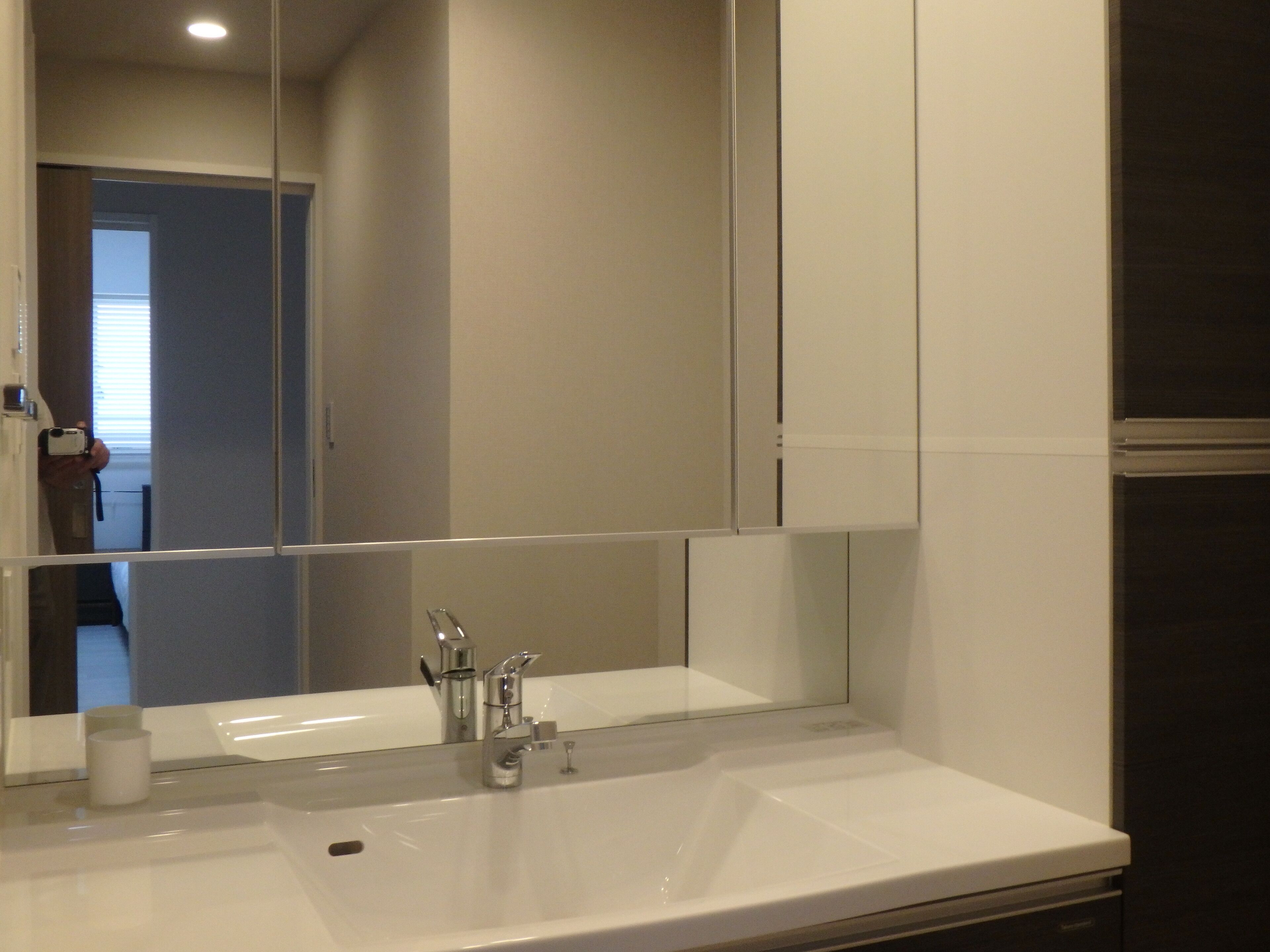 A bathroom with a large mirror, a white sink, and a modern faucet.