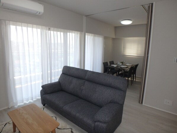 A modern living room with a grey sofa, a wooden coffee table, and a dining area with a table set for four.
