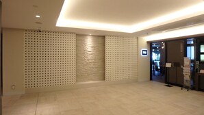 A spacious lobby with a modern design, featuring a patterned wall, a textured wall, and a reception area with a counter and informational signs. - buransiera naha akebono puremisuto 1009 (Naha)