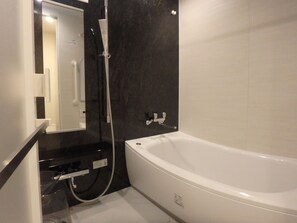 Une salle de bain moderne avec une baignoire blanche, une douchette à main et un robinet mural.