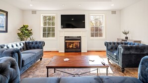 Una sala de estar con chimenea, dos sofás azules, una mesa de centro y un televisor sobre la chimenea.