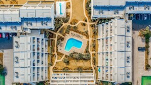 An aerial view of a hotel with multiple floors, a central swimming pool, and surrounding greenery.