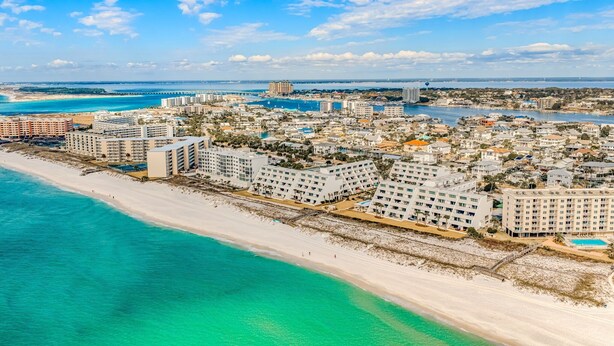 A coastal cityscape with beachfront hotels, a bridge, and a clear sky.