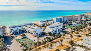 An aerial view of a coastal hotel complex with multiple buildings, parking areas, and palm trees.