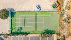 Eine Vogelperspektive auf einen Tennisplatz mit umliegendem Parkplatz und Grünflächen.