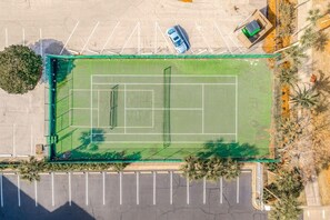 Eine Vogelperspektive auf einen Tennisplatz mit umliegendem Parkplatz und Grünflächen.