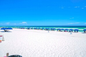 Ein Strand mit Reihen aus blauen Sonnenschirmen und Liegestühlen.