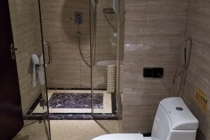 Un baño con ducha acristalada, inodoro y secamanos.