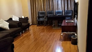 A living room with a wooden floor, a sofa set, a coffee table, and a TV. - Qianhao Hotel (Tongzi County)