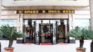 A hotel entrance with a revolving door, potted plants, and a sign with Chinese characters. - Qianhao Hotel (Tongzi County)