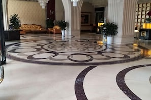 Um lobby com piso padronado circular, balcão de recepção e áreas de estar.