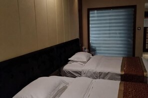 Habitación de hotel con dos camas, cabecera oscura y puerta cerrada con persianas horizontales.