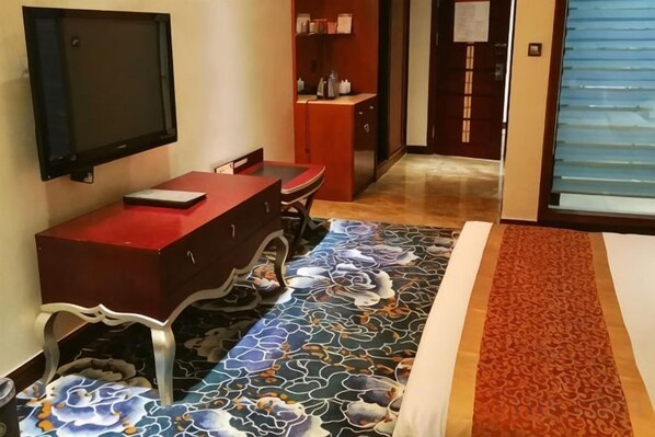 Habitación de hotel con un escritorio rojo, un televisor de pantalla plana montado en la pared, una alfombra estampada y una puerta corredera que da a otra habitación.