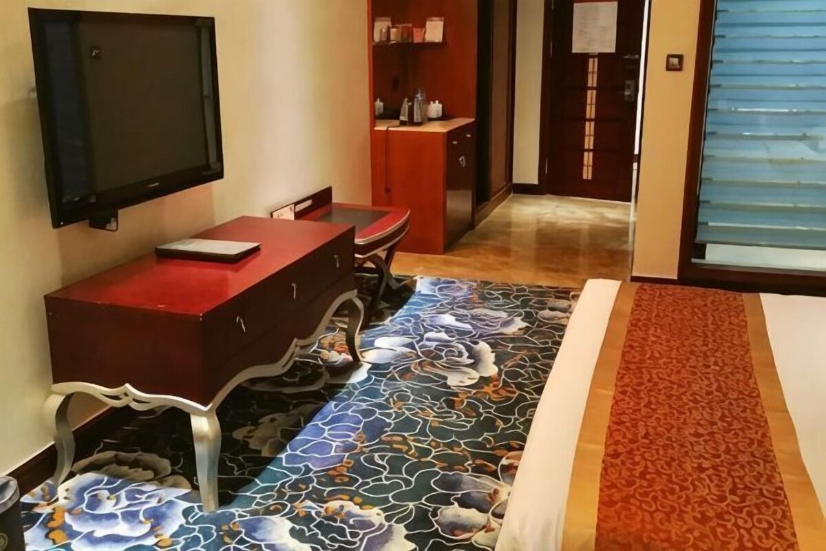 A hotel room with a TV mounted on the wall, a red desk, and a patterned carpet.