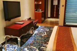 A hotel room with a TV mounted on the wall, a red desk, and a patterned carpet. - Qianhao Hotel (Tongzi County)