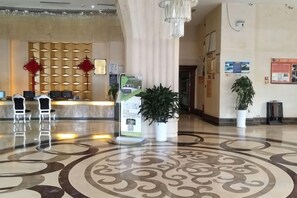 Un vestíbulo de hotel con mostrador de recepción, sillas, una planta en maceta y un suelo estampado.