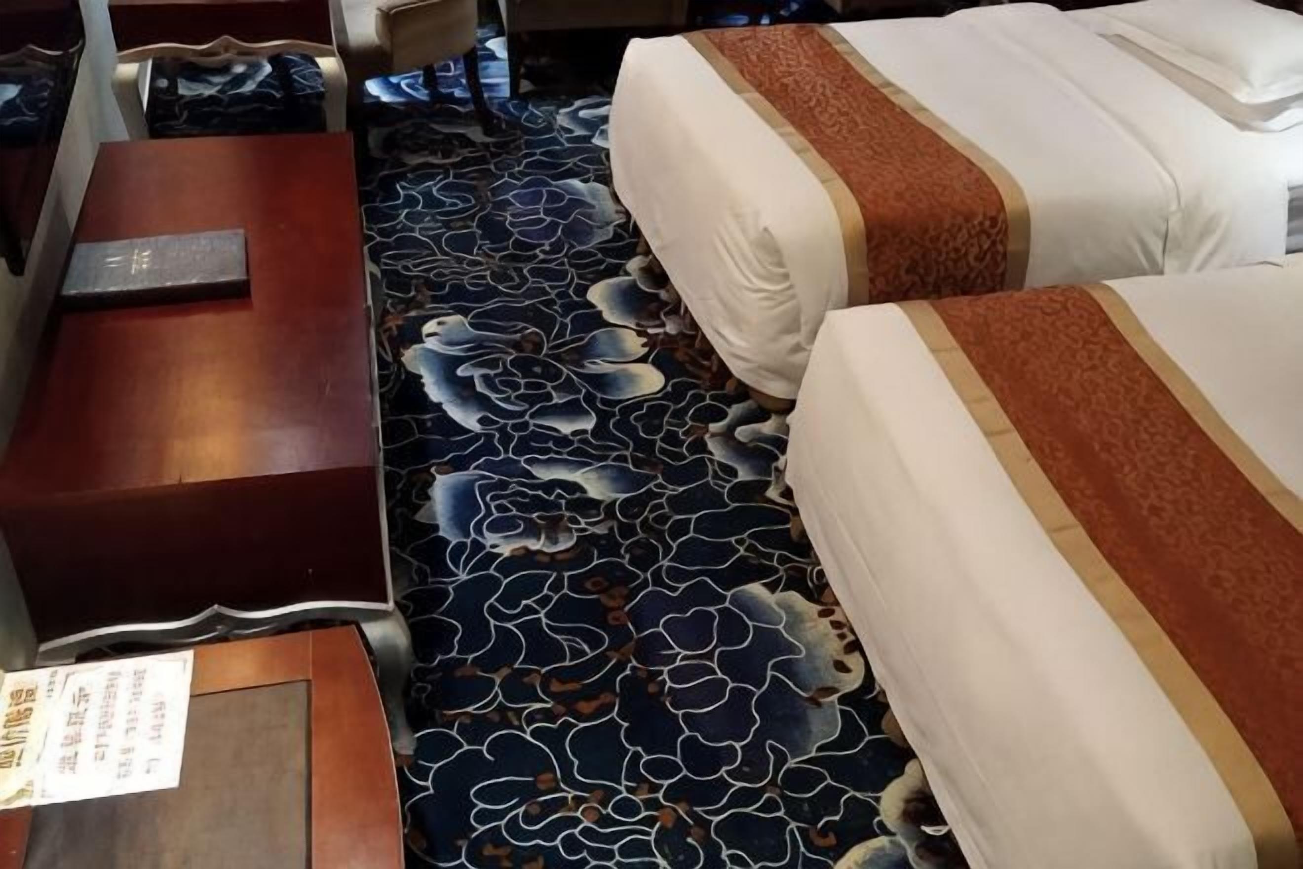 A hotel room with two beds, a wooden nightstand, and a patterned carpet.