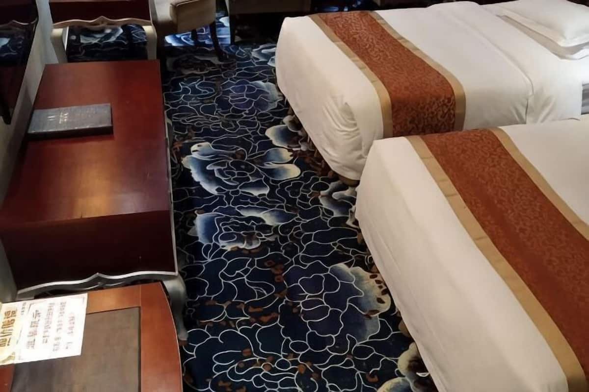 A hotel room with two beds, a wooden nightstand, and a patterned carpet.