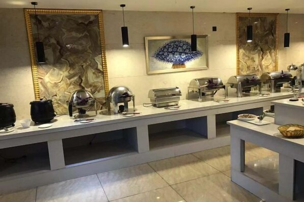 Montaje tipo bufé con distintas estaciones de comida, una pared de mármol y una obra de arte central.