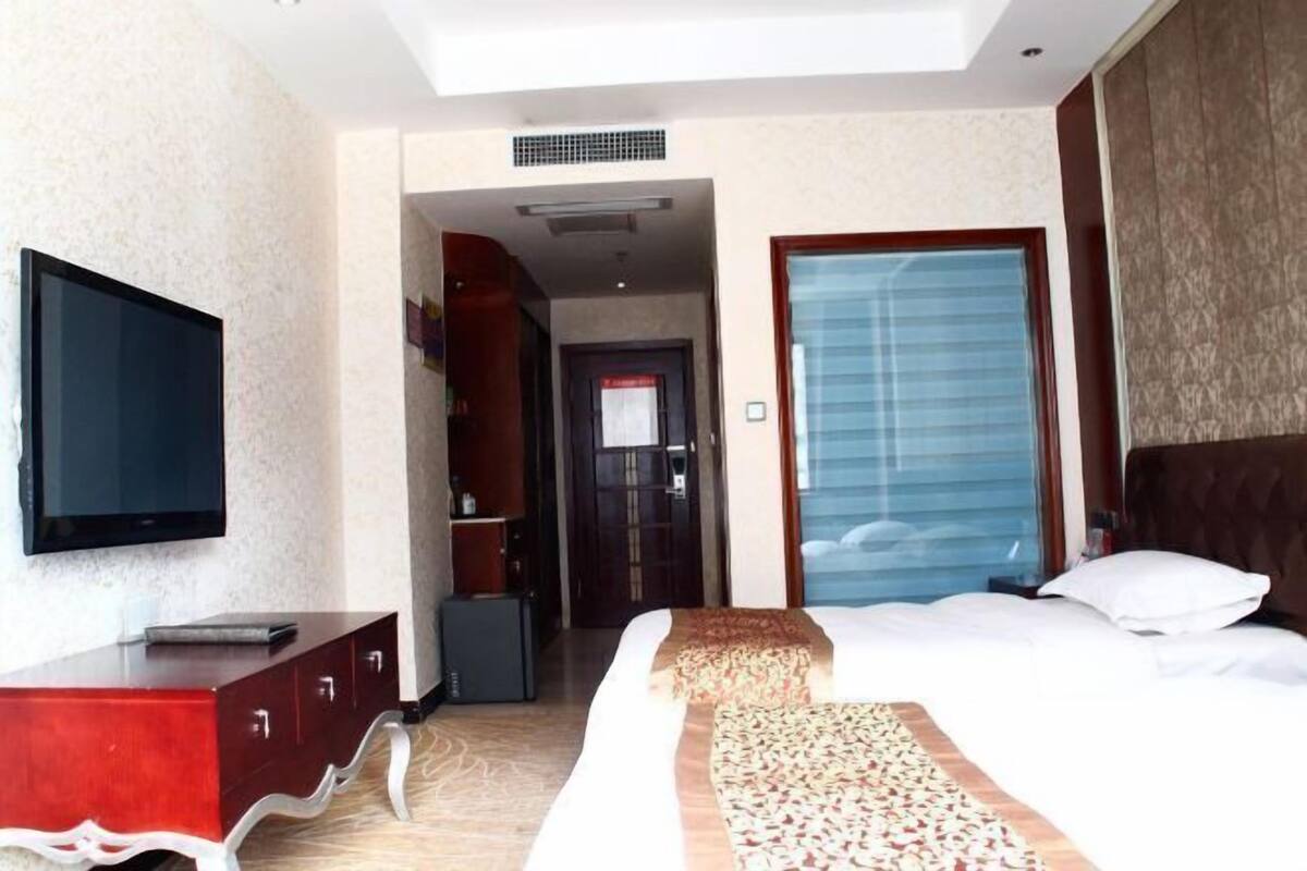 A hotel room with a bed, a TV, a wardrobe, and a door leading to a hallway.