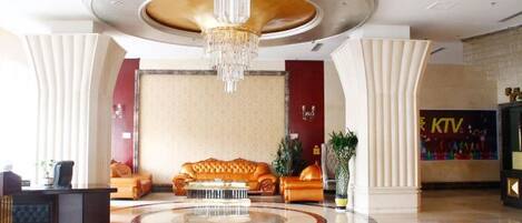 A hotel lobby with a central seating area, a chandelier, and a reception desk.