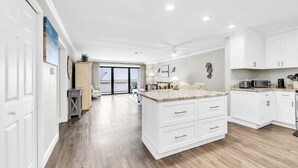 A spacious kitchen with white cabinetry, a large island, and a dining area with chairs.