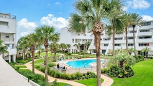 A hotel courtyard with a swimming pool, palm trees, and a well-maintained lawn.