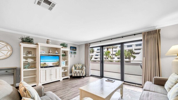 A living room with a TV, sofa, table, and a view of palm trees through large windows.