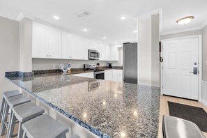Cocina moderna con armarios blancos, encimera de granito, refrigerador de acero inoxidable y microondas.
