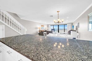 A spacious living area with a kitchen island, a staircase, and a view to the outside. - Aegean 305: Spacious Beachfront Retreat w/ Pool and Gulf Views (Destin)