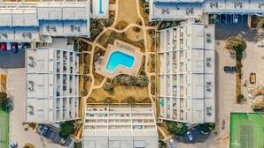 Vista aérea de un hotel con varias construcciones, una piscina central y zonas de estacionamiento circundantes.