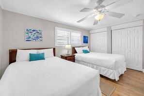 Una habitación de hotel con dos camas, un ventilador de techo, una ventana con persianas y una puerta.