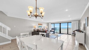 A spacious living area with a dining table, white chairs, and a chandelier.
