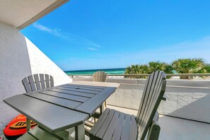 A patio with a table and two chairs, overlooking a beach with palm trees and the ocean. - Aegean 309: Spacious 3BR Condo with Gulf Views (Destin)