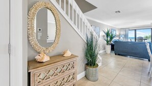 A modern living room with a staircase, a large mirror, decorative shells, and a potted plant. - Aegean 309: Spacious 3BR Condo with Gulf Views (Destin)