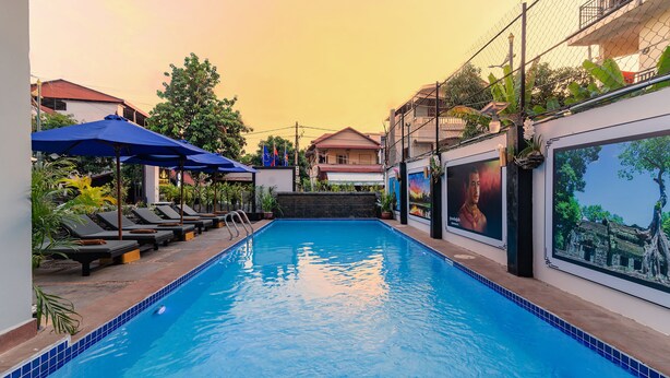 Una piscina con tumbonas y sombrillas, rodeada de edificios y vegetación.