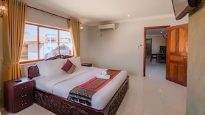 Habitación de hotel con una cama grande, una mesita de noche de madera, un televisor montado en la pared y vistas al exterior a través de una ventana con cortinas.
