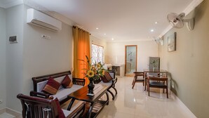 Sala de estar con sofá, mesa de comedor, sillas, un jarrón con flores, aire acondicionado instalado en la pared, ventilador de techo y un cuadro en la pared.