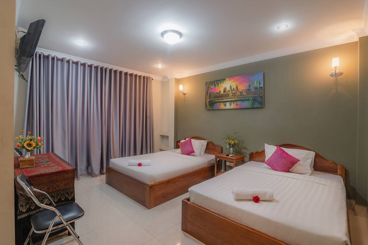 Quarto de hotel com duas camas, uma mesa com cadeira, televisão e um quadro na parede.