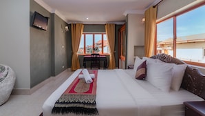 Habitación de hotel con una cama grande, una mesita con una silla, un televisor montado en la pared y vistas al exterior.