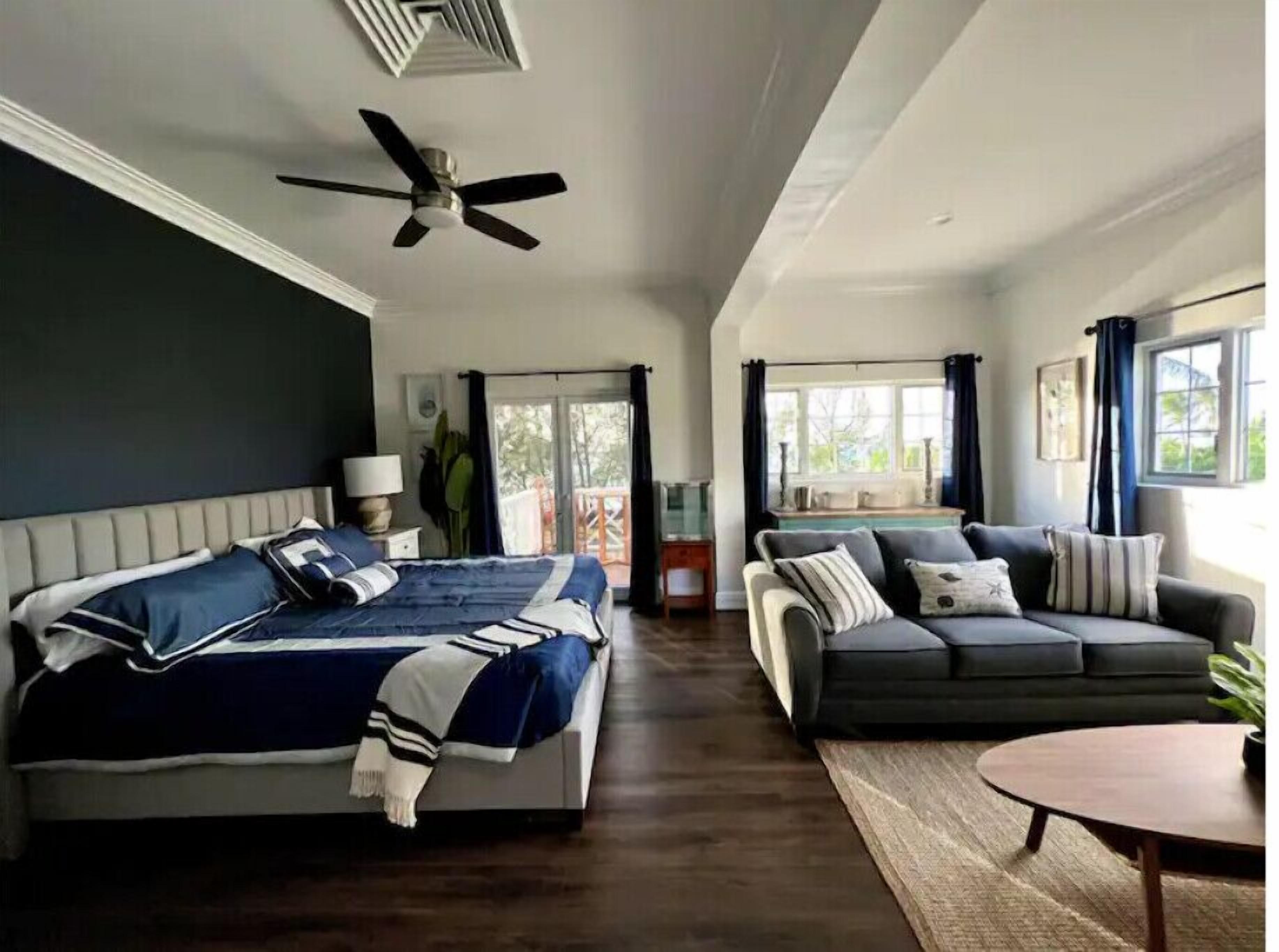 A spacious room with a bed, a sofa, a small table, and a ceiling fan.